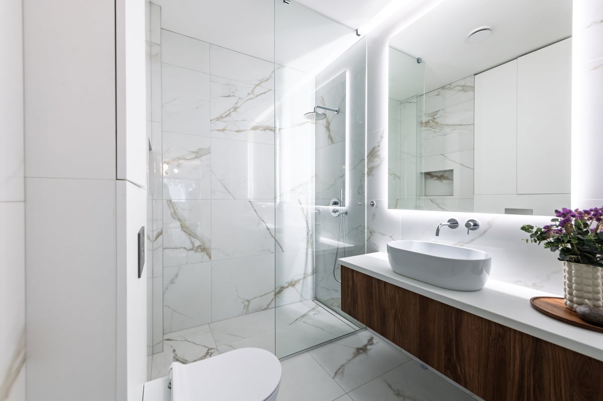 Baño moderno con mármol, lavabo flotante de madera y espejo retroiluminado
