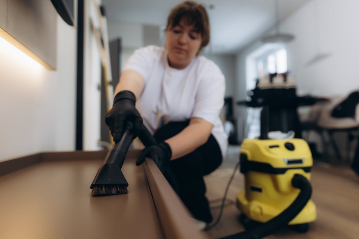 Profesional de limpieza con guantes aspirando una superficie del hogar